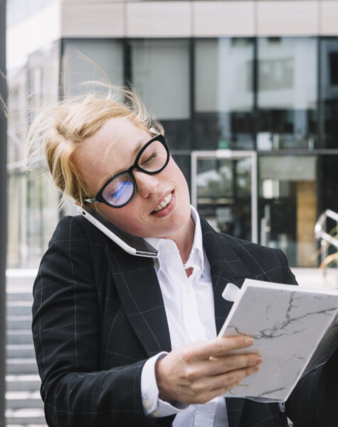 smiling-young-businesswoman-talking-cell-phone-holding-diary-hand
