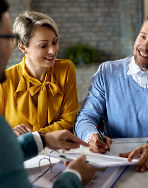 Happy couple signing paperwork while having a meeting with financial advisor in the office.